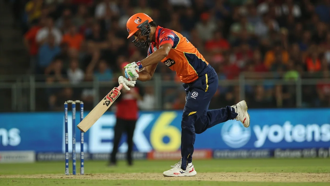 Tight sideline frame of a right-handed batter playing through the off side at the crease, bat raised mid-stroke, with a slip fielder and the wicketkeeper standing back against the Arun Jaitley stadium backdrop